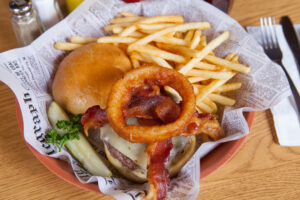 Delicious burger with bacon, onion ring, cheese served with a pickle and french fries from A Pine Restaurant in Pequot Lakes, Minnesota.